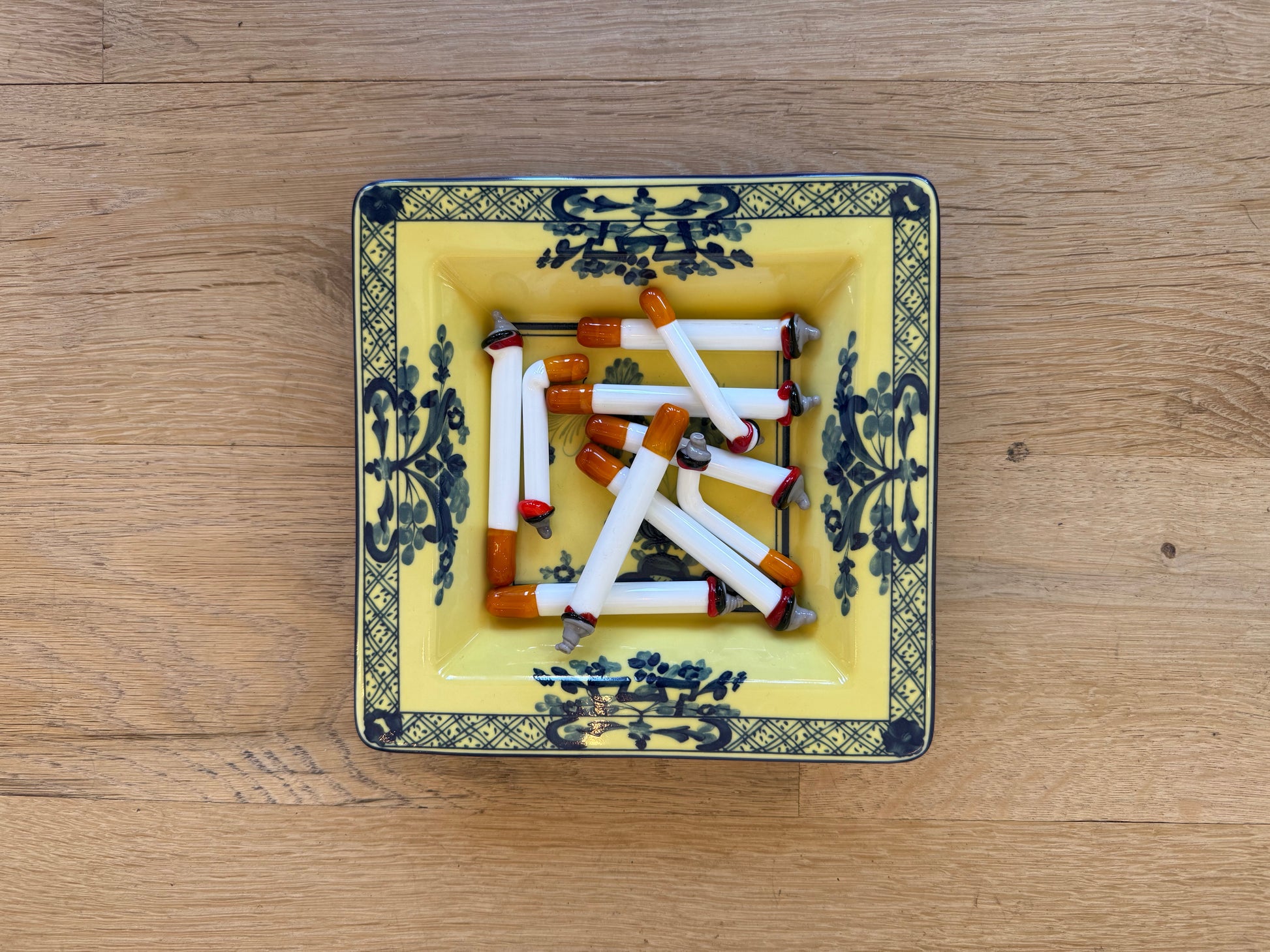 Murano glass cigarettes in a yellow and blue porcelain tray, overhead view