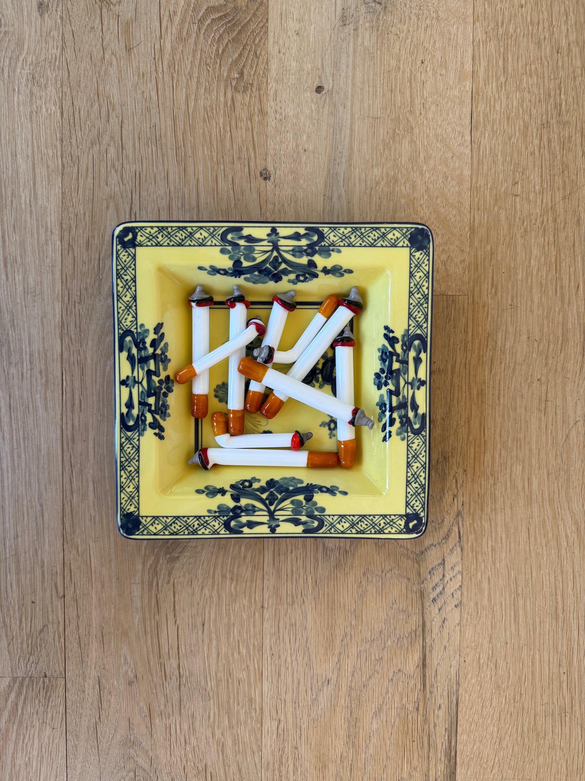 Murano glass cigarettes in a yellow and blue porcelain tray on a wood table